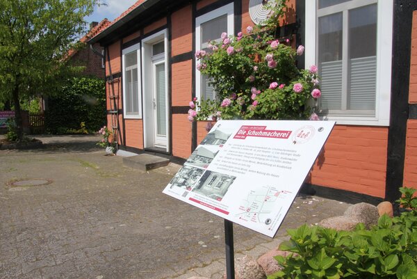 Blick auf eine Infotafel zur Geschichte des dahinter befindlichen Schumacher-Hauses in Stöcken / Landkreis Uelzen