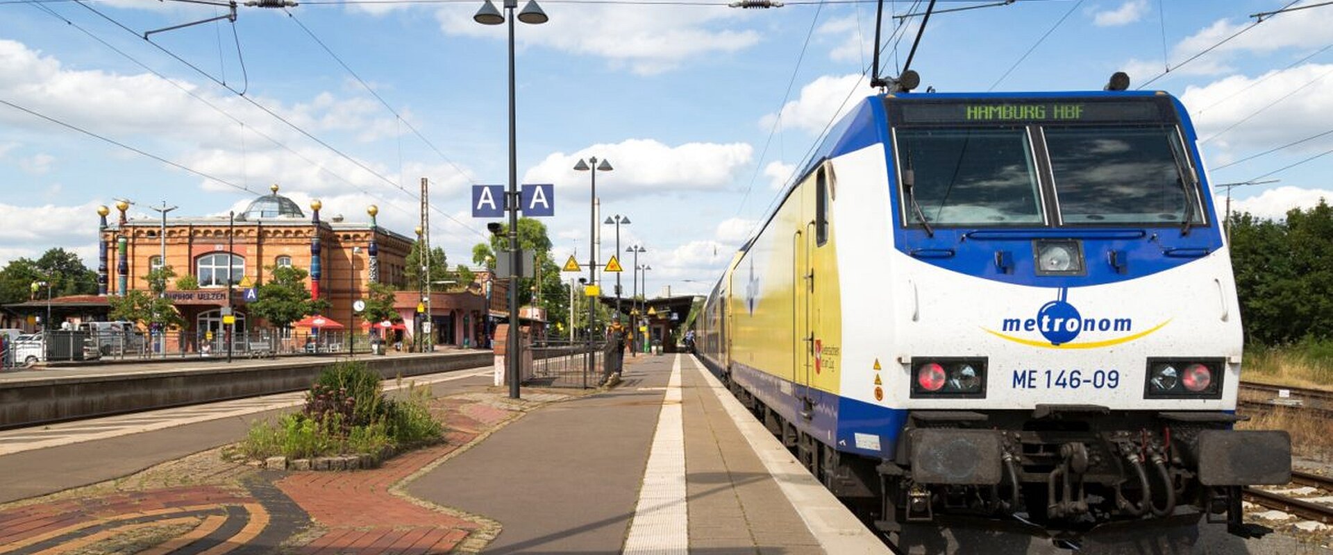 Blick auf den Triebwagen eines metronom-Zuges, links im Hintergrund der Hundertwasser-Bahnhof in Uelzen