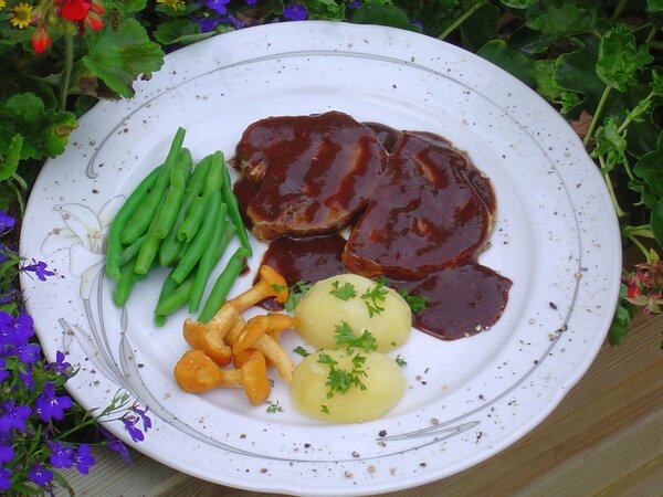 Ein Speiseteller mit Salzkartoffeln, Pfifferlingen, Bohnen und Heidschnuckenbraten mit Soße