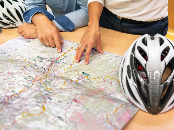 Die Hände eines Paares zeigen auf eine Fahrradstrecke, die auf der vor ihnen ausgebreiteten Fahrradkarte abgebildet ist. 